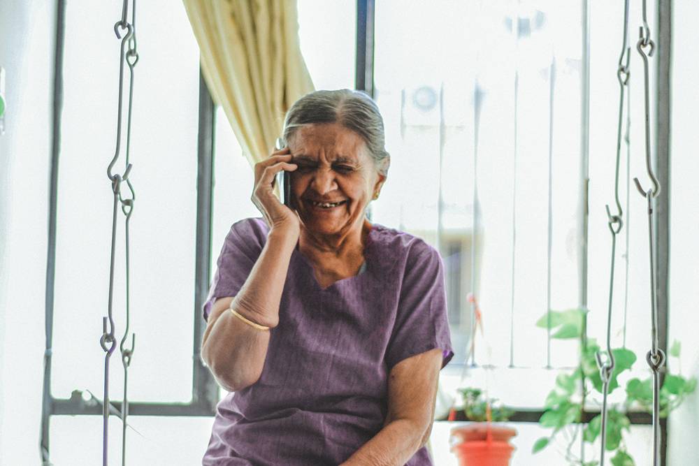 elderly woman inside her home joyously using a soft phone to call her loved ones